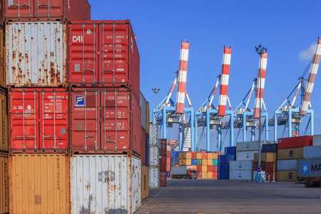 Port dock with container ship and Various brands and colors of shipping containers stacked in a holding platform waiting for loading.のeditorial素材
