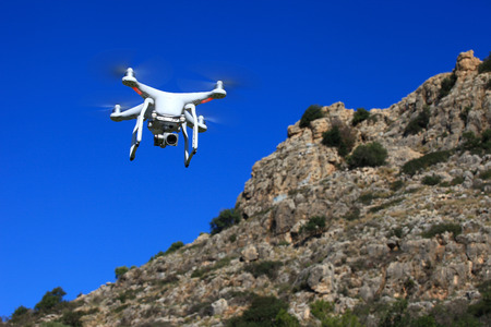 White drone equipped with high resolution 4K video camera hovering in mid air with a blurred cliff in the backgroundの写真素材