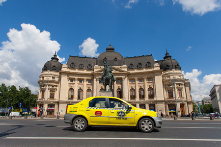 Central University Library and King Carol's statue in Bucharest with local yellow taxi passing byのeditorial素材