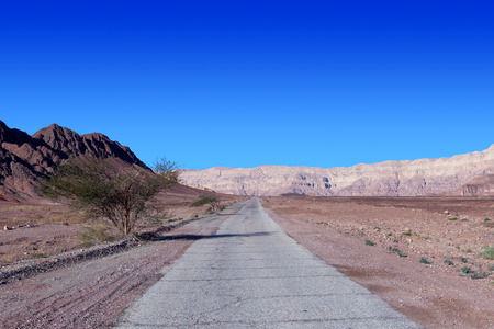 Empty desert road with mountains and blue sky in the backgroundの写真素材