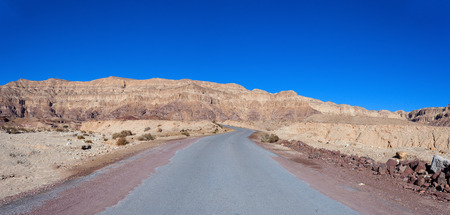 Empty desert road with mountains and blue sky in the backgroundの写真素材