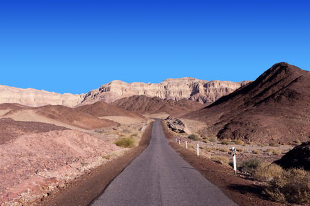 Empty desert road with mountains and blue sky in the backgroundの写真素材