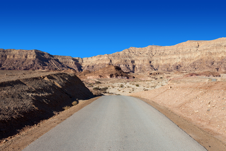 Empty desert road with mountains and blue sky in the backgroundの写真素材