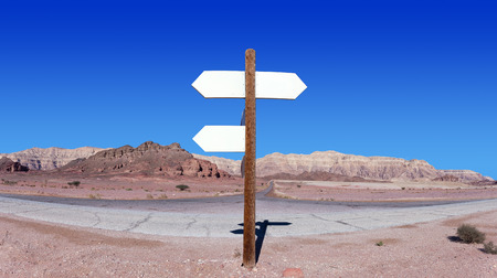 Empty arrow shaped signs in the middle of the desert with blue sky and mountains in the backgroundの写真素材