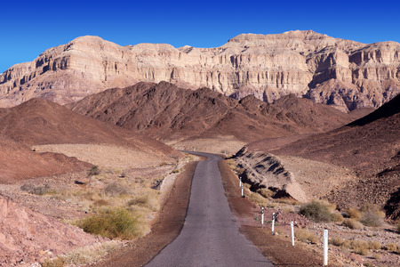 Empty desert road with mountains and blue sky in the backgroundの写真素材