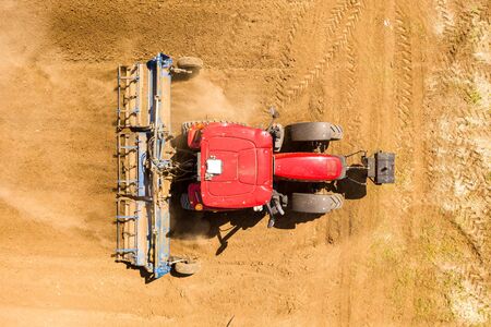 Red Tractor Cultivating a large field located near a residential area.の写真素材