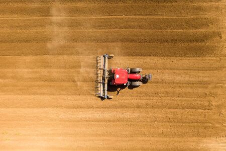 Red Tractor Cultivating a large field located near a residential area.の写真素材