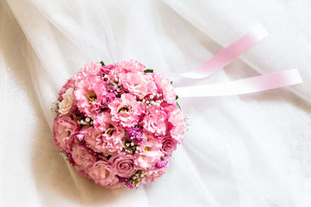 A bouquet of pink flowers on the skirt of a white wedding dressの写真素材