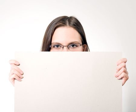young brunette woman in glasses holding a white card with both hands above her mouthの写真素材