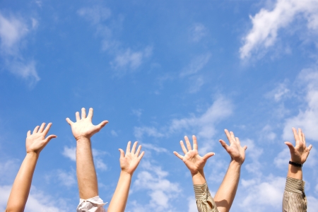 Hands rised up in air across blue skyの写真素材