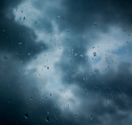 Rain drops on window glass across stormy clouds background