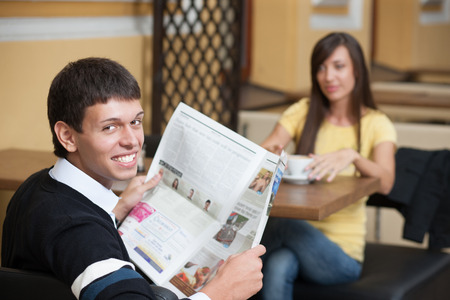 Read news and drink coffee. Young beautiful man posing across table with cup of coffeeの写真素材