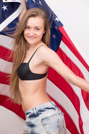 Thin and slender American model with flag in photostudio. Sexy girl in black underwear and blue jeans shorts.の写真素材