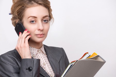 Portrait of young serious business lady discussing companys difficult situation. Woman dressed in grey business suit carrying documents,files, etc.の写真素材