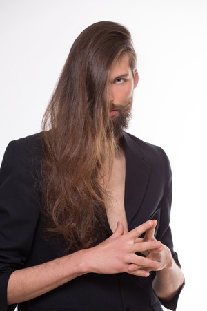 Long-haired transexual posing in black mens suit. Transexual looking seriuos isolated on white background.の写真素材