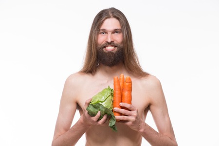 Naked body vegetarian smiling for photo camera. Man carrying cabbage and carrots isolated on white background.の写真素材