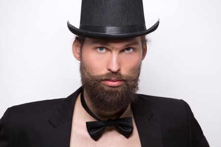 Portrait of bearded model with top hat. Handsome man with bow tie and black jacket looking severe.の写真素材