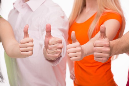 Four thumbs meaning "no problems any more". Young people showing thumbs up isolated on white background.の写真素材