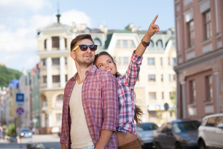 Portrait of young couple in the city centre. Girl pointing out in the beautiful blue sky, man is smiling.の写真素材