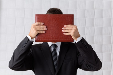 Young businessman hiding behind the register in front of him. Successful man going to outdistance competitors isolated on cream background.の写真素材