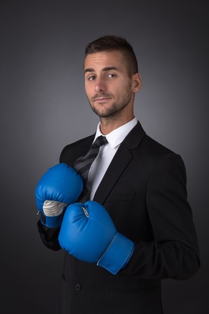 Businessman with blue boxing gloves punch to the goal, business concept. Serious man in business suit looking straight at the camera.の写真素材