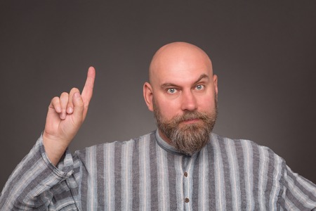 Bearded jailbird pointing out on dark grey background. Bold man in shirt in line havinf serious and...