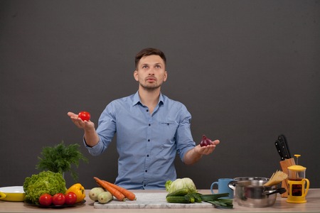 Handsome man looking upwards with a pensive thoughtful look while standing in his kitchen. Chef is going to cook and prepare a meal from a variety of fresh vegetables.の写真素材