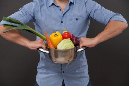 Close-up picture of pan with fresh vegetables. Man in blue shirt demonstrating products for meals he is goint to prepare and cook.の写真素材