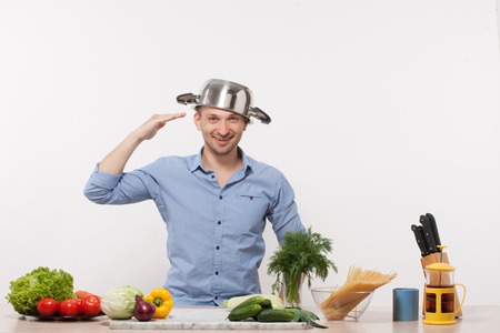 Chef enjoying in his kitchen isolated on white. Man with pan on his head in blue shirt smiling and and going to prepare smth with fresh vegetables.の写真素材