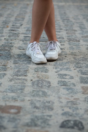 Close-up picture of woman's legs in white sneakers outdoors. Woman demonstrating her expensive jogging shoes.の写真素材