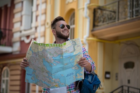 European hipster man in sunglasses smiling and carrying a guide in his hands. Bearded man with backpack going to visit all the city's sightseeings.の写真素材