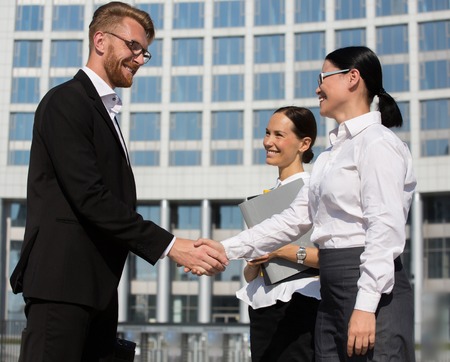 Businesspeople shaking hands. Two confident persons shaking hands and smiling, thecollegue keeping all documents near them.の写真素材
