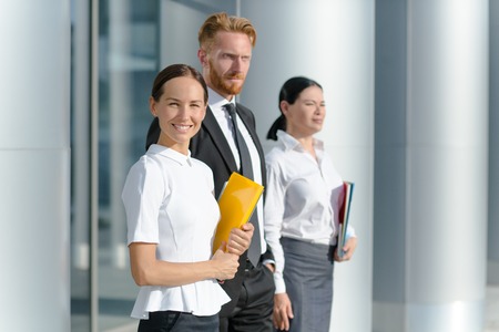 Three businesspeople welcoming you. Woman in white shirt with yellow folder smiling isolated on her collegues.の写真素材