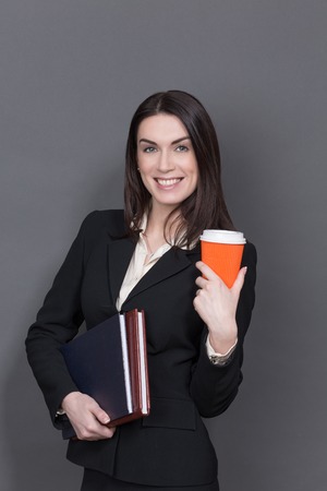 Portrait of business lady keeping a cup of delicious coffee. Smiling woman wiyj long black hair posing with documents.の写真素材