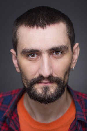Portrait of serious hipster bearded man in plaid shirt and T-shirt. Short-haired man with earring...