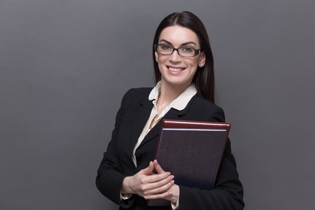 Business lady smiling in glasses. Pretty model in black business suit carrying documents and files in her hand.の写真素材