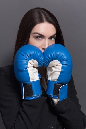 Business lady keeping hands in blue with white boxing gloves. Long0haired woman hiding behind her hands isolated on grey.の写真素材