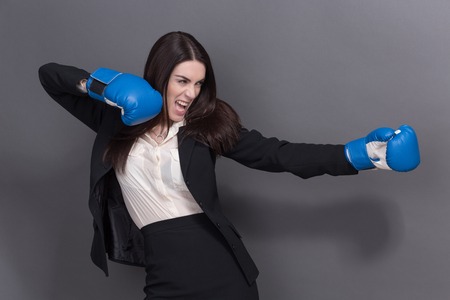 Portrait of angry woman isolated on grey. Business woman is wearing boxing gloves and black business suit on grey background.の写真素材