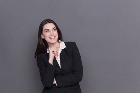 Business lady smiling and looking away. Long-haired woman in black business suit and white shirt touching her chin.の写真素材