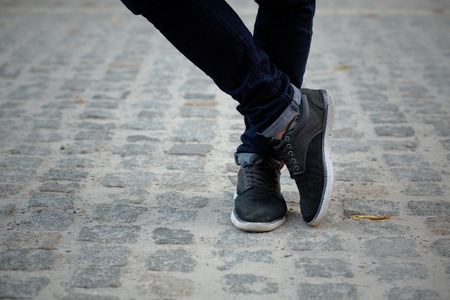 Close-up picture of man who crossed his legs. Man in black jeans and sneakers enjoying daytime in the city.の写真素材