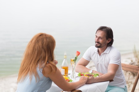 Beautiful couple sitting face to face in the restaurant. People holding each other's hands, they are having lunch isolated on the sea.の写真素材