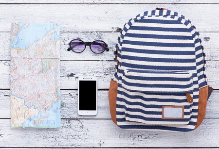 Photo of summer objects isolated on wooden background. Map, sunglasses, smart phone and striped bag are ready for your travelling.の写真素材