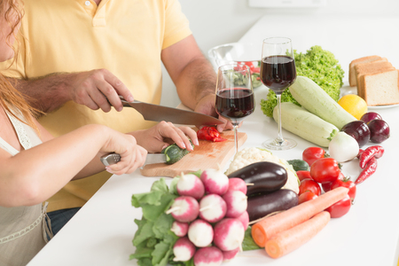 Close-up portrait of man and woman cooking vegetables salad in the kitchen. There carrots, tomatoes, cucumbers, etc. on the table.の写真素材