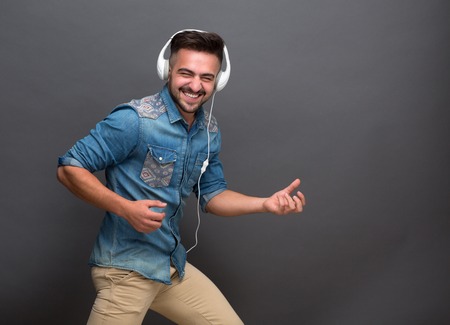 Handsome hipster man enjoying his life listening to best music using earphones. Stylish and fashionable man smiling for the camera and dancing.の写真素材