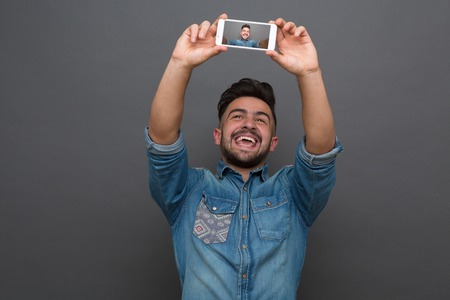 Handsome bearded hipster man making selfies and showing his teeth. Short-haired man in jeans shirt posing in photo studio.の写真素材