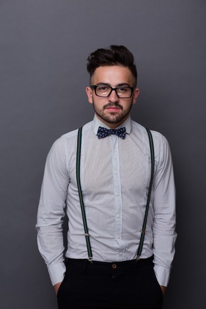 Portrait of serious hipster man posing for photographer in studio. Man in glasses standing with his hands in pockets.の写真素材