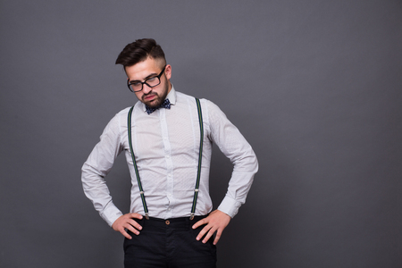 Serious hipster man posing with his hands on hips in studio. Sad man in glasses looking down isolated on grey background.の写真素材