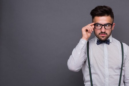 Portrait of serious hipster man keeping his glasses isolated on grey. Handsome man in white shirt looking away in studio.の写真素材