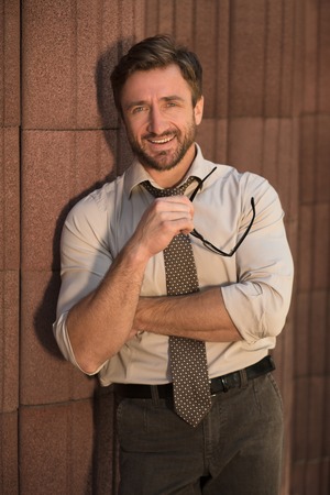 Hipster businessman happy smiling outdoors. Handsomeshort-haired man put off his glasses and looking at the camera over wall with red columns.の写真素材