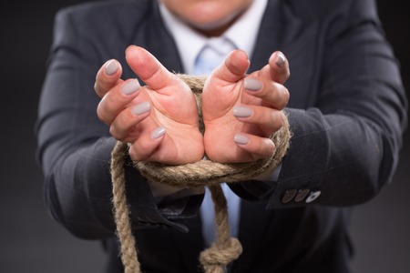 Close-up picture of female hands tied up with strong rope. Businesswoman ingrey business suit trying to escape from these problems.の写真素材